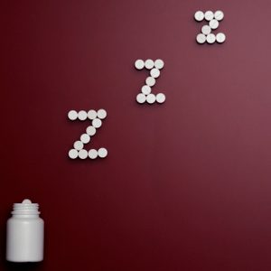 pill bottle and pills in zzz formation on dark red background