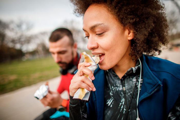 Young sportswoman enjoying in a protein bar with her partner while sitting on a bench in a city park