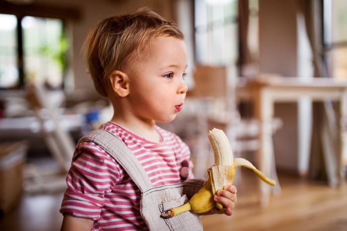 young toddler eating a banana at home