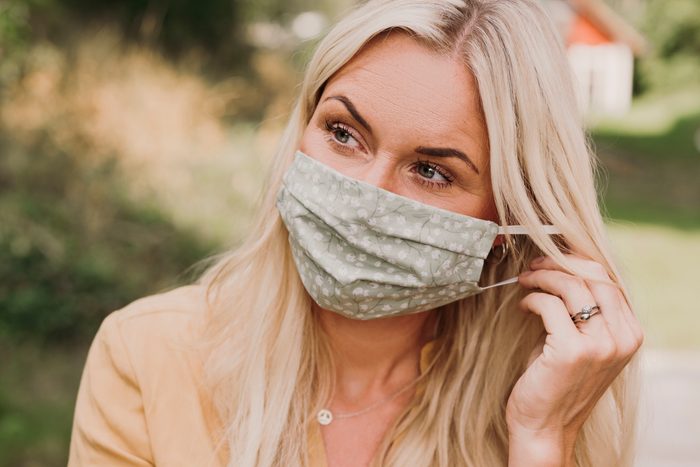 Content woman putting on wearing a protective mask in times of corona