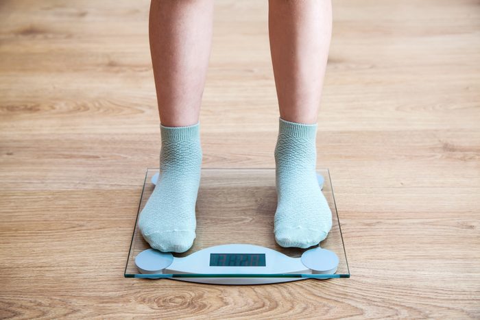 Low Section Of Woman Wearing Socks While Standing On Weighing Scale