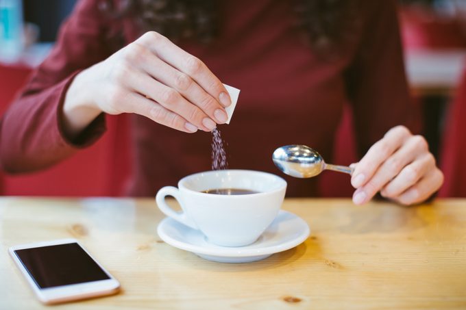 Mani di donna che versano zucchero nel caffè nero - ragazza seduta al tavolo con caffè espresso e smartphone - controllo dell'indice glicemico e del sangue per il diabete - eccesso di zucchero bianco nel concetto di cibo
