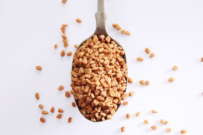 Fenugreek Seeds In Spoon Over White Background