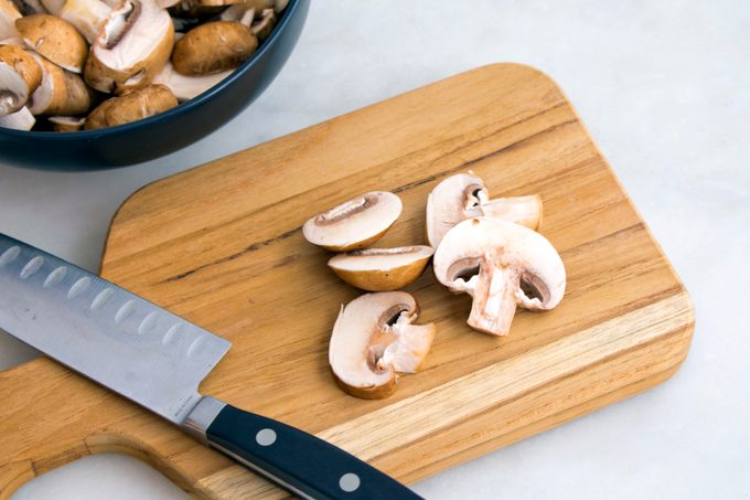 Slicing cremini mushrooms on a wooden cutting board