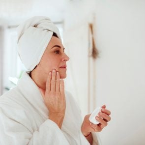 Mature woman in a bathroom at home applying moisturizer