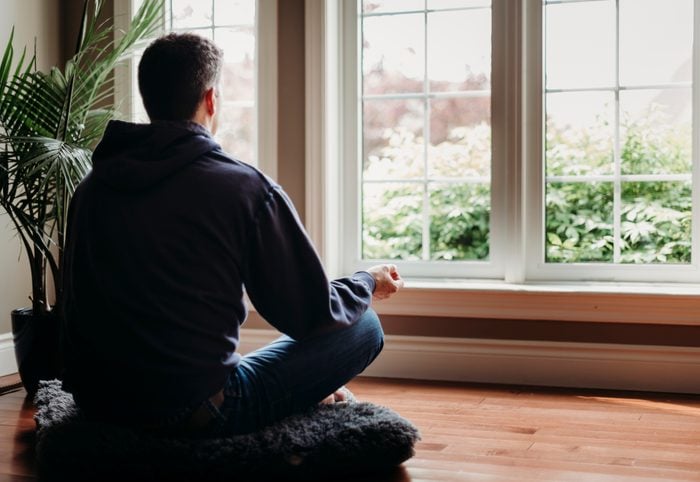 Mann, der drinnen auf dem Boden sitzt und vor den Fenstern meditiert.