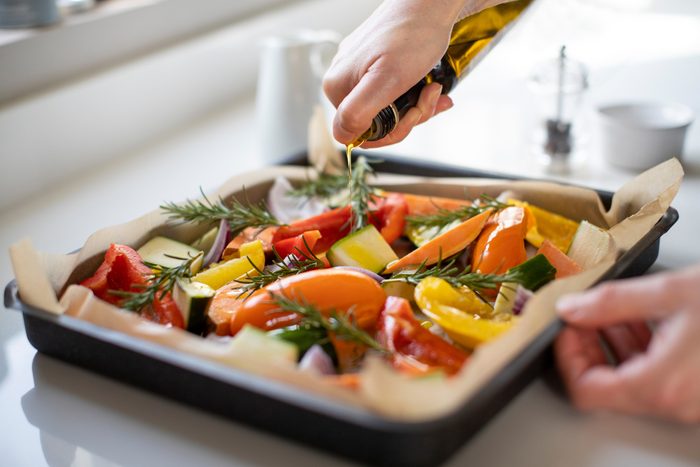 drizzling olive oil on pan of vegetables