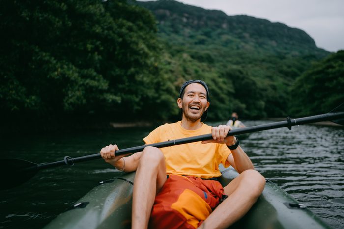 Man paddling kayak in mangrove river and laughing, Iriomote, Japan