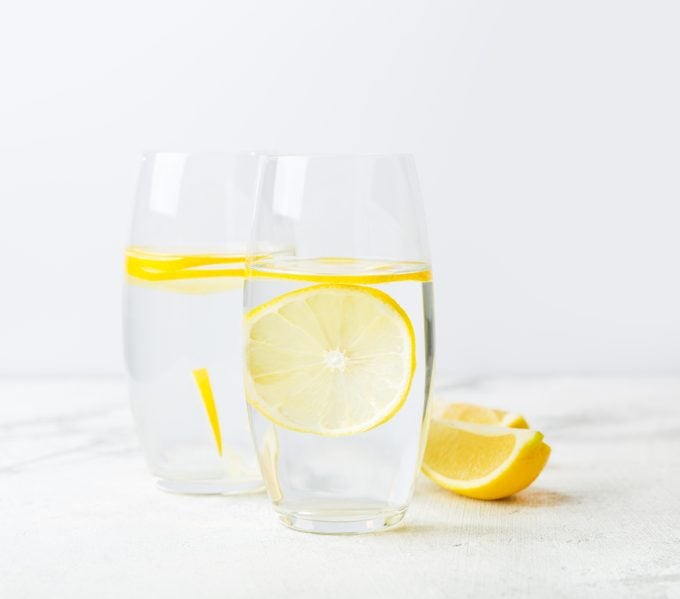two glasses of lemon water on white background
