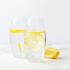two glasses of lemon water on white background