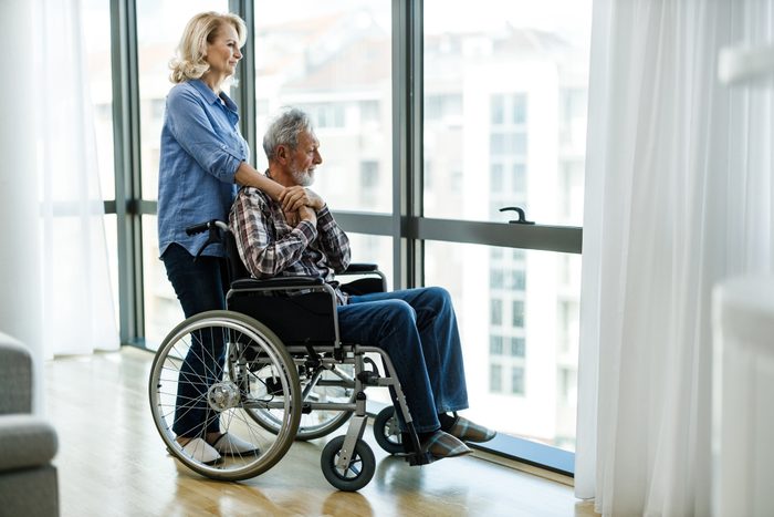 Mature woman with man in wheelchair looking through window.