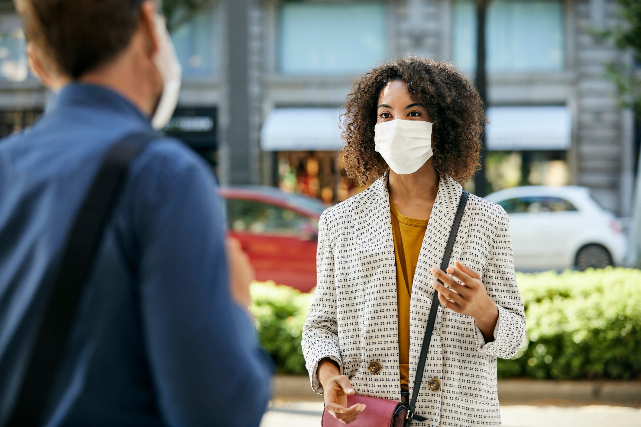 Businesswoman Wearing Protective Face Mask Talking To Male Coworker During COVID-19 Pandemic In City