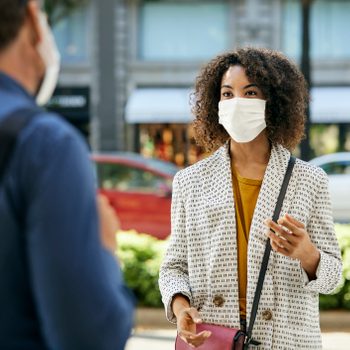 Businesswoman Wearing Protective Face Mask Talking To Male Coworker During COVID-19 Pandemic In City