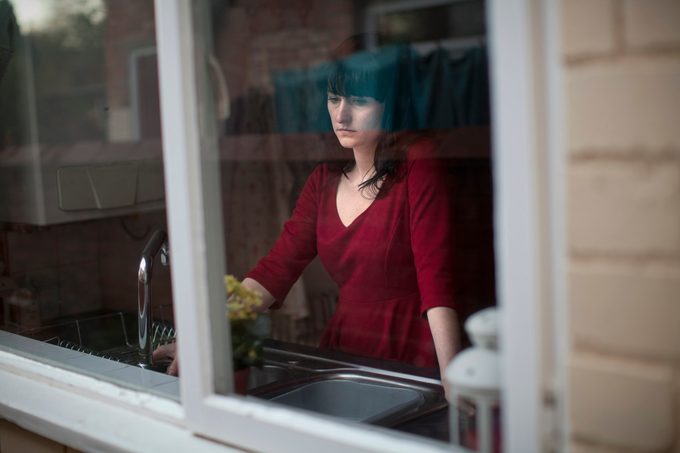 sad woman at kitchen sink, looking out window