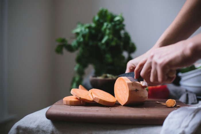 A woman is slicing a sweet potato to use in a sweet potato