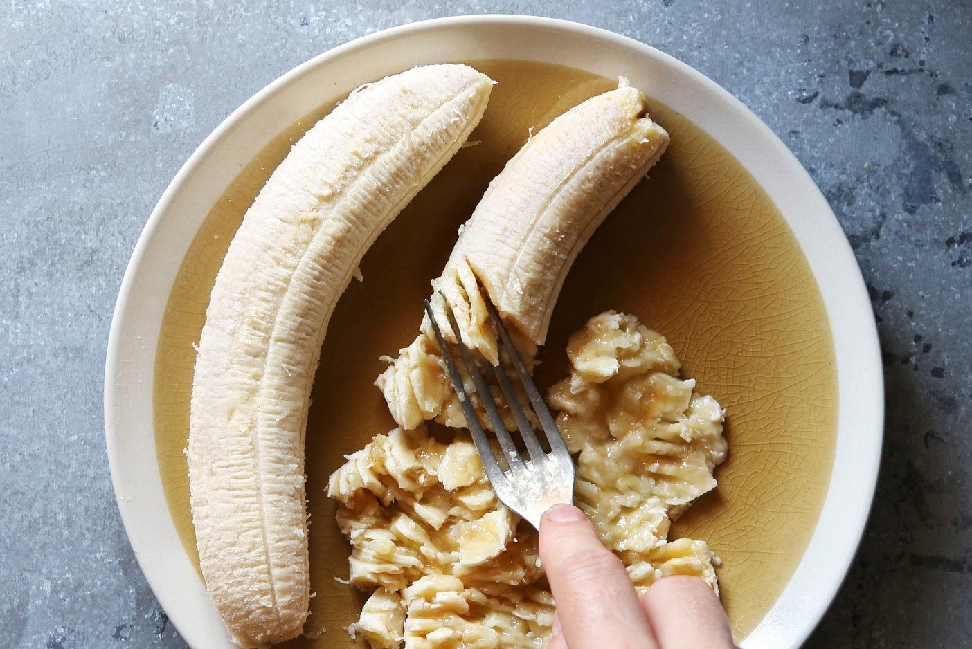 Female hand mashing banana with a fork.Top view