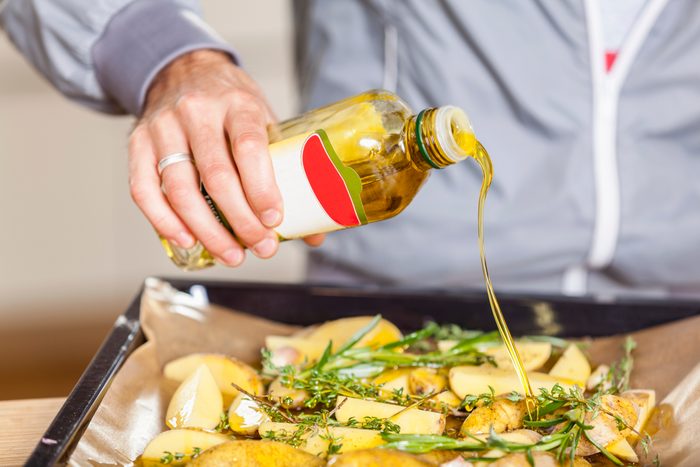 Pouring oil over potato wedges on baking tray