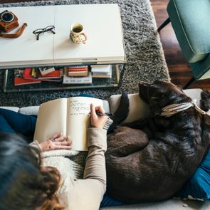 woman on sofa with dog writing in journal
