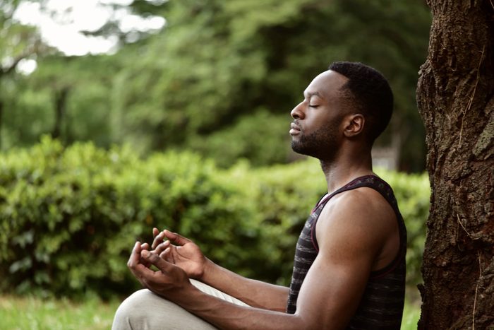 young man meditating outside under a tree