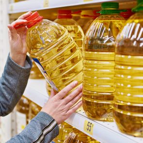 woman taking large bottle of oil off of shelf at grocery store