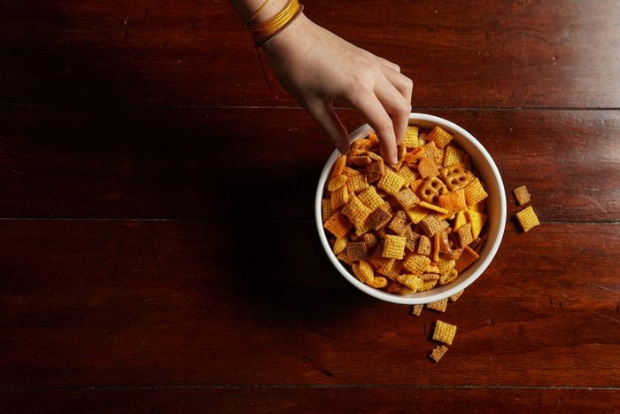 Hand reaching for bowl of junk food snacks - flat lay copy space