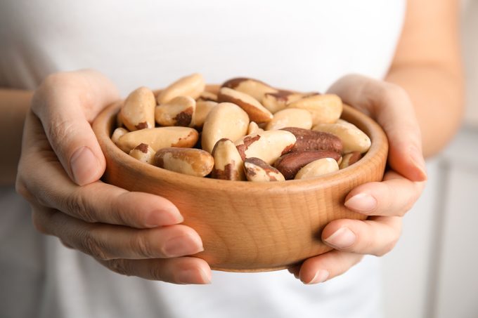 Woman holding bowl with Brazil nuts on blurred background, closeup