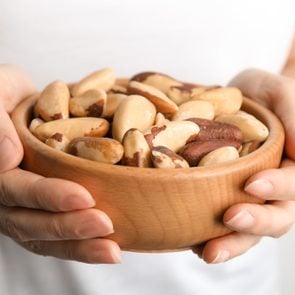 Woman holding bowl with Brazil nuts on blurred background, closeup