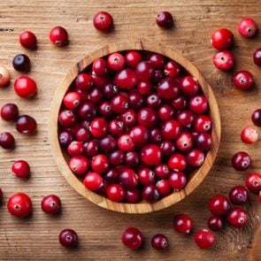 Fresh raw cranberry in wooden bowl on rustic table top view.