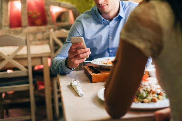 Man checking messages while having dinner in a restaurant