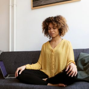 young woman sitting on couch at home doing breathing exercises