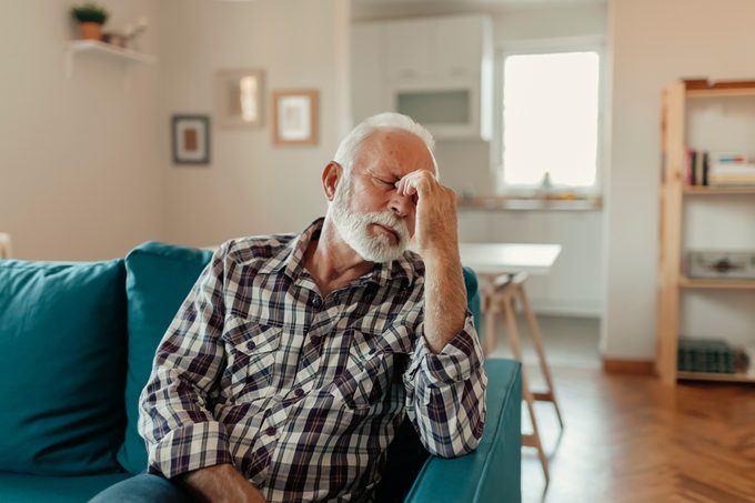 mature man with headache sitting on couch at home