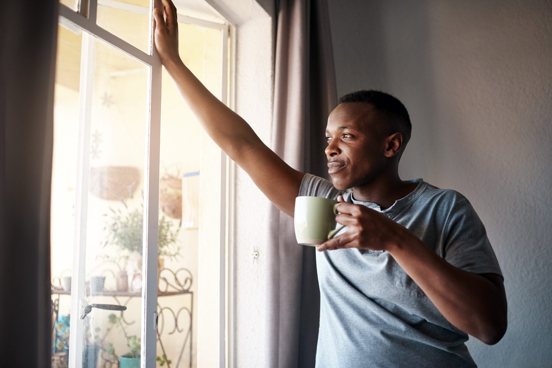 man looking out window with a cup of coffee
