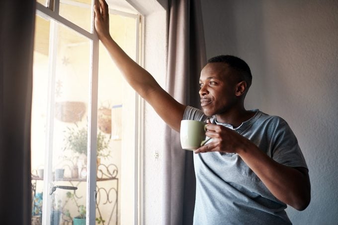 man kijkt uit raam met een kopje koffie