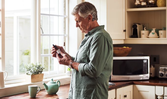 mature man holding bottle of CBD oil in kitchen