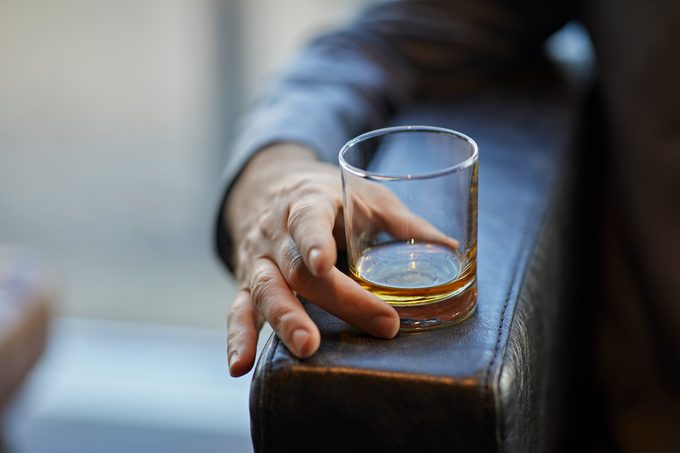 Close-up of man with whiskey glass on armrest of a leather chair