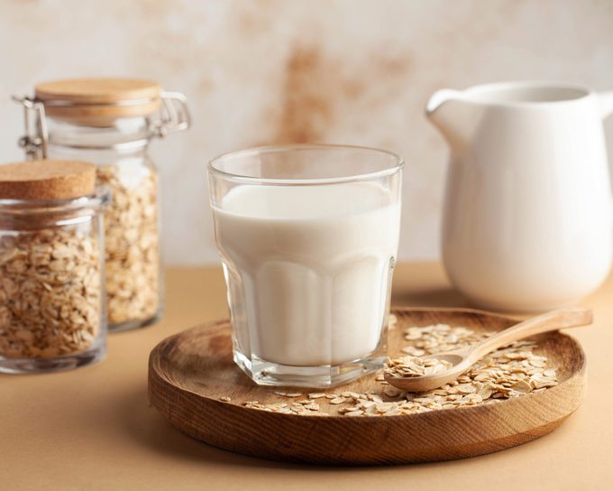 Oat milk in a glass, surrounded by jars of oats