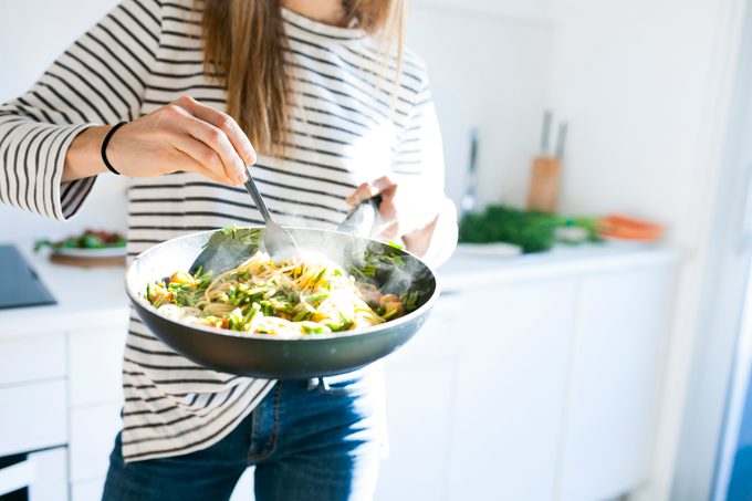 woman holding pan with vegetable-filled pasta dish