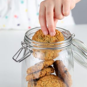 Clear glass jar full of cookies, child's hand taking one of the cookies out of the jar.
