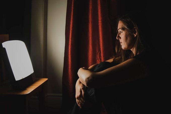 Profile of woman sitting looking at light therapy lamp in a dark room