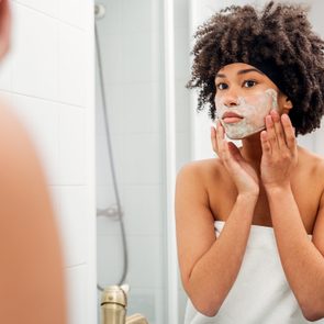 Teenage Girl Applying Facial Mask While Looking In Mirror At Bathroom