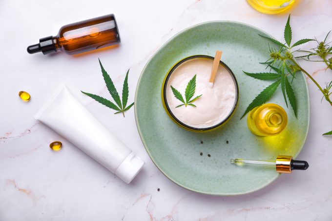 Cosmetics with cannabis oil on a turquoise plate on a light marble background