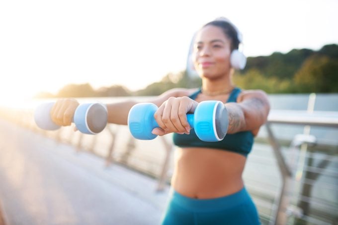 Woman holding blue barbells while building arm muscles
