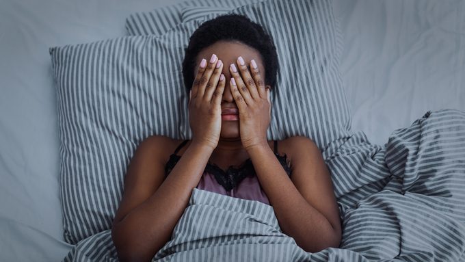 African american girl closed eyes with hands in bed