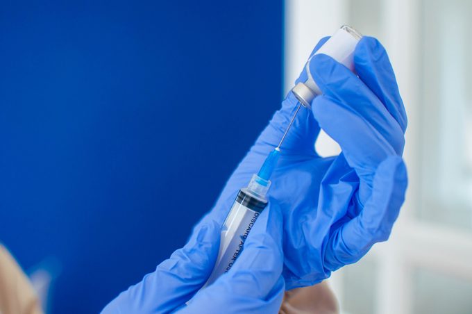 A young doctor in blue protective glove is holding a medical syringe and vial