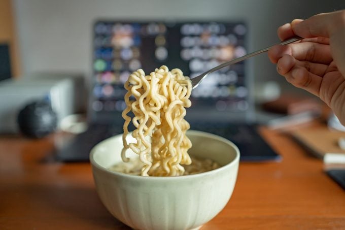 Mangiare spaghetti istantanei a un tavolo da lavoro