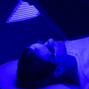 Young woman having blue LED light facial therapy treatment in beauty salon. Beauty and wellness