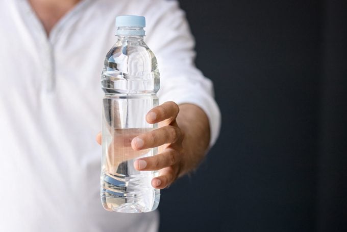 Midsection Of Man Holding Water Bottle Against Black Background