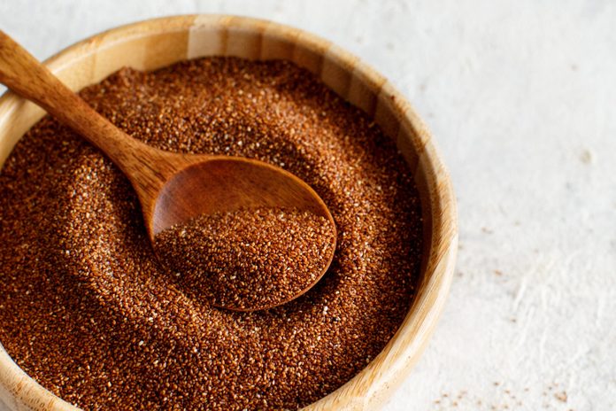 Uncooked teff grain with a wooden spoon close up