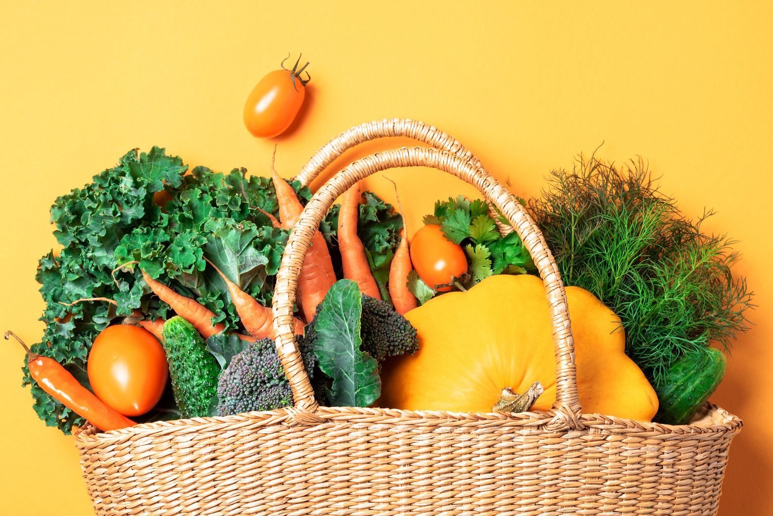 Straw basket with organic vegetables over trendy yellow background. Healthy food, vegetarian diet. Eco friendly, zero waste, plastic free concept.