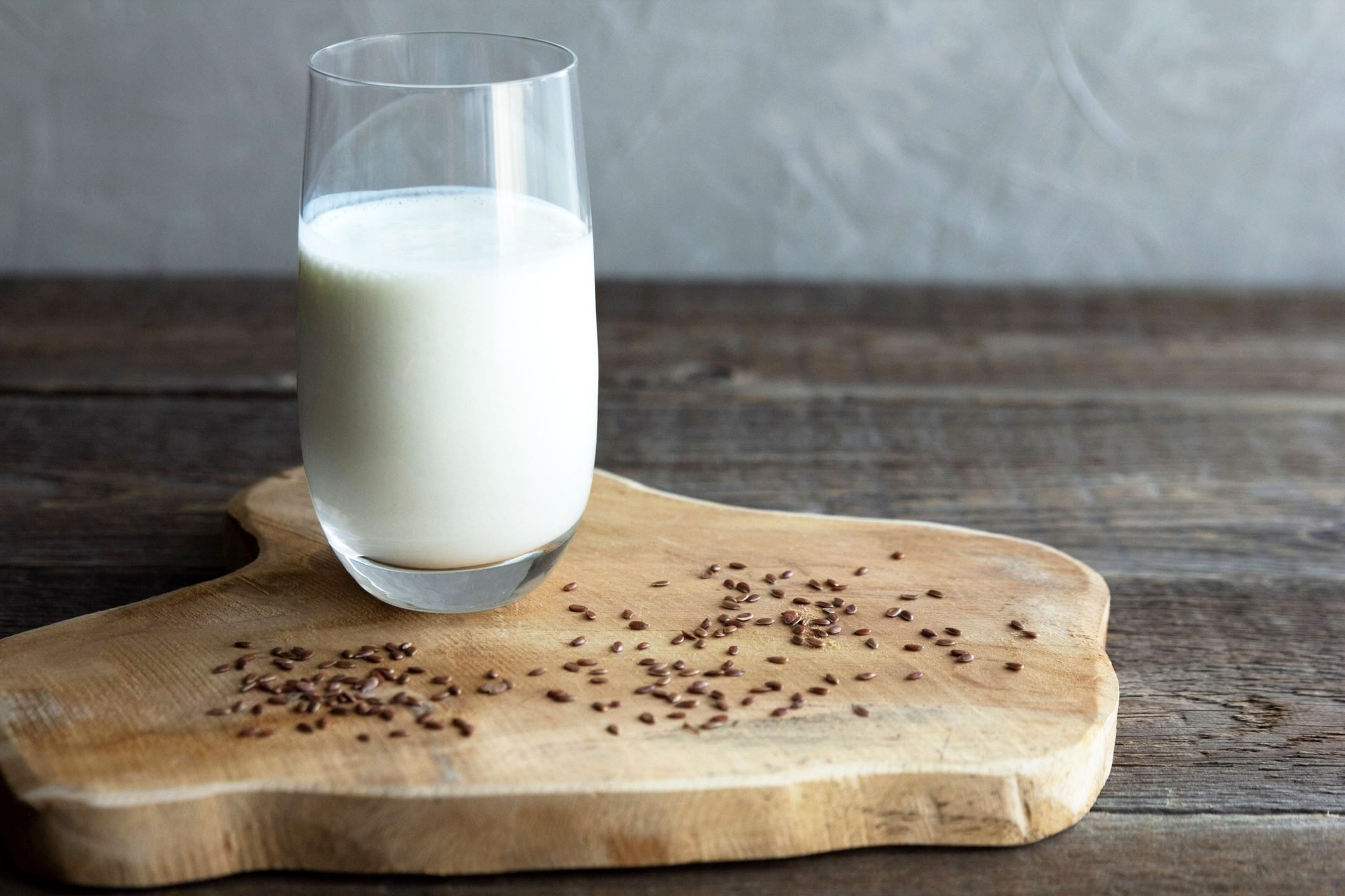 A glass cup of flax milk stands on a wooden board and flax seeds are scattered nearby. Wood background. Healthy snack. Copy space